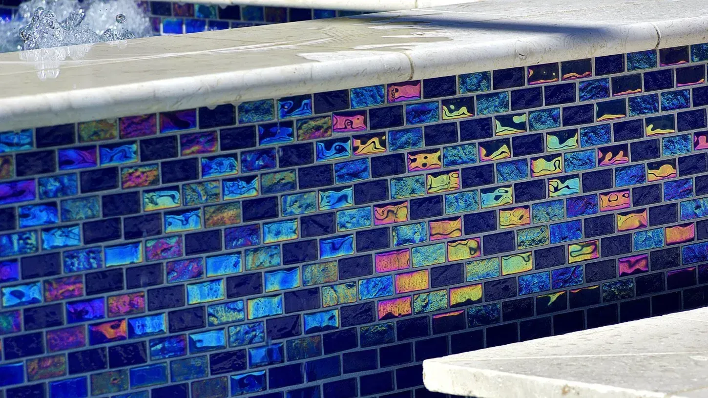 Poolside wall with iridescent blue, purple, and yellow mosaic tiles.