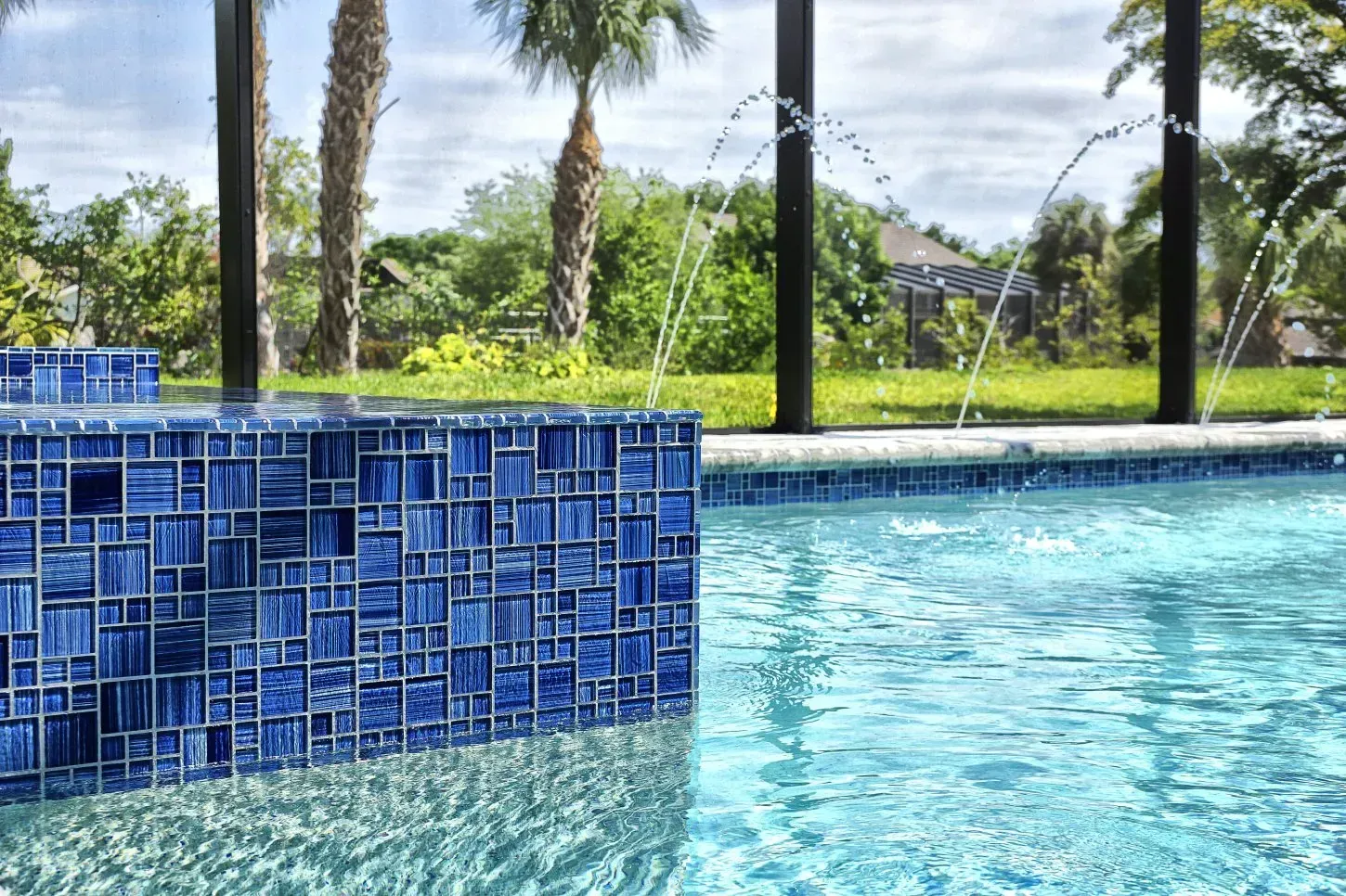 Blue tiled pool with fountains against a backdrop of palm trees and a sunny sky.