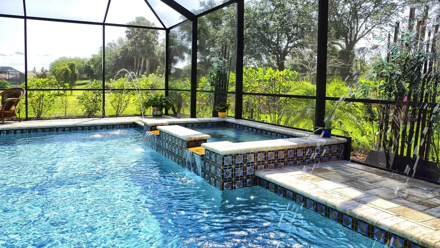 Swimming pool and spa within a screened enclosure, surrounded by greenery.