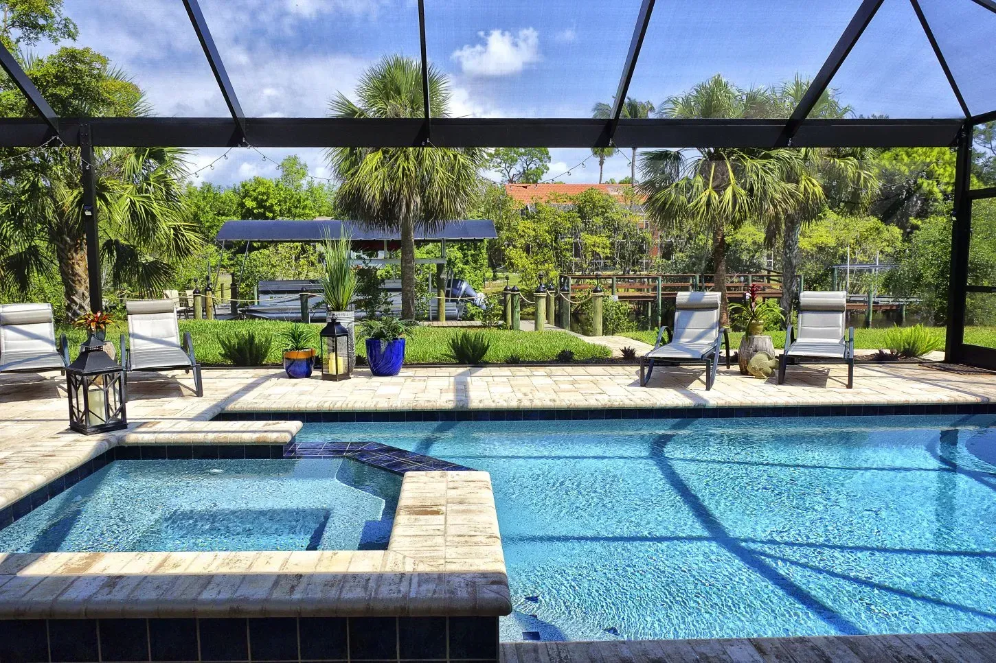 Pool area with blue water, lounge chairs, lush greenery, and a screened enclosure.