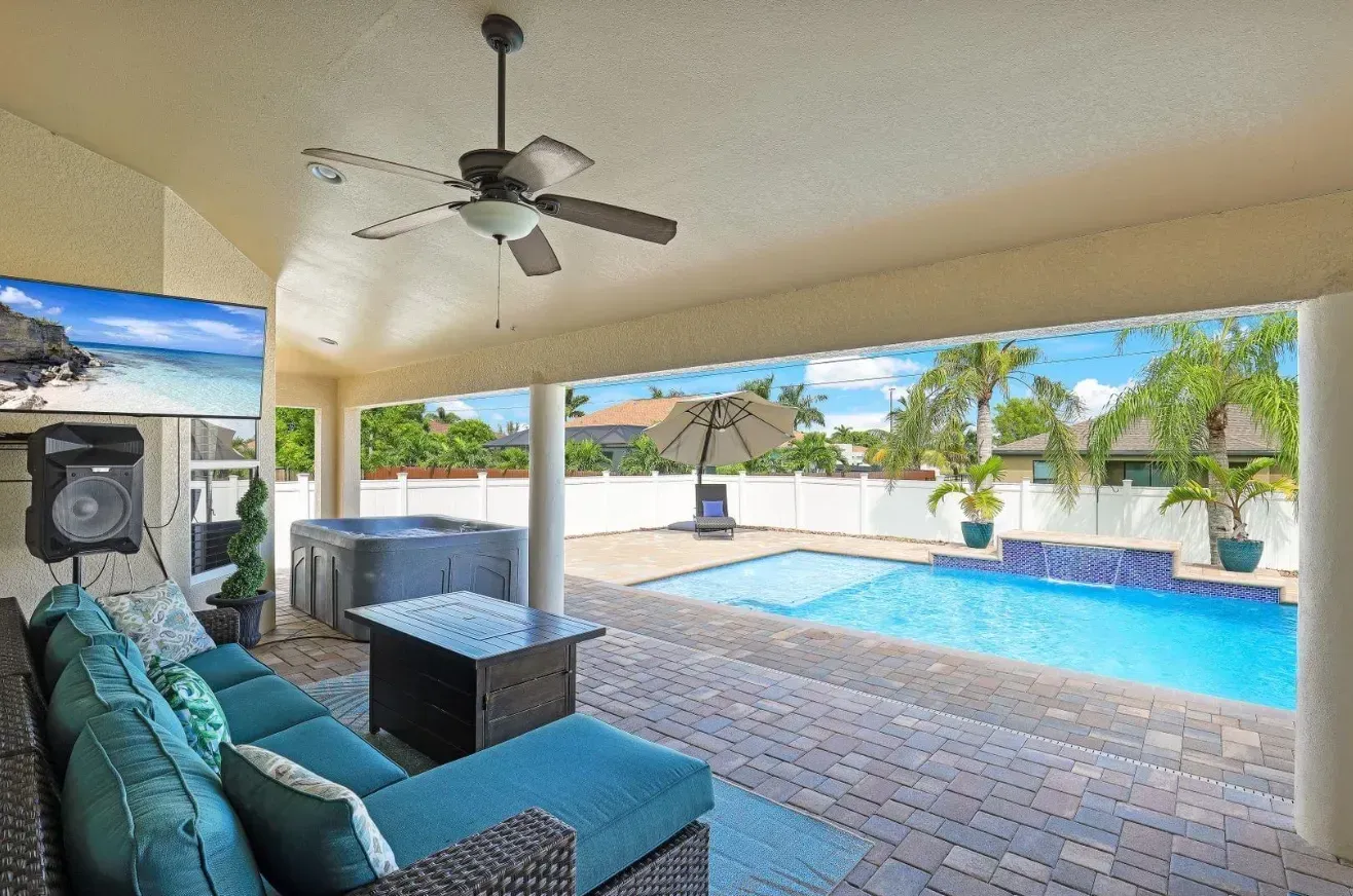 Patio with turquoise furniture, TV, pool, spa, and ceiling fan, view to backyard.