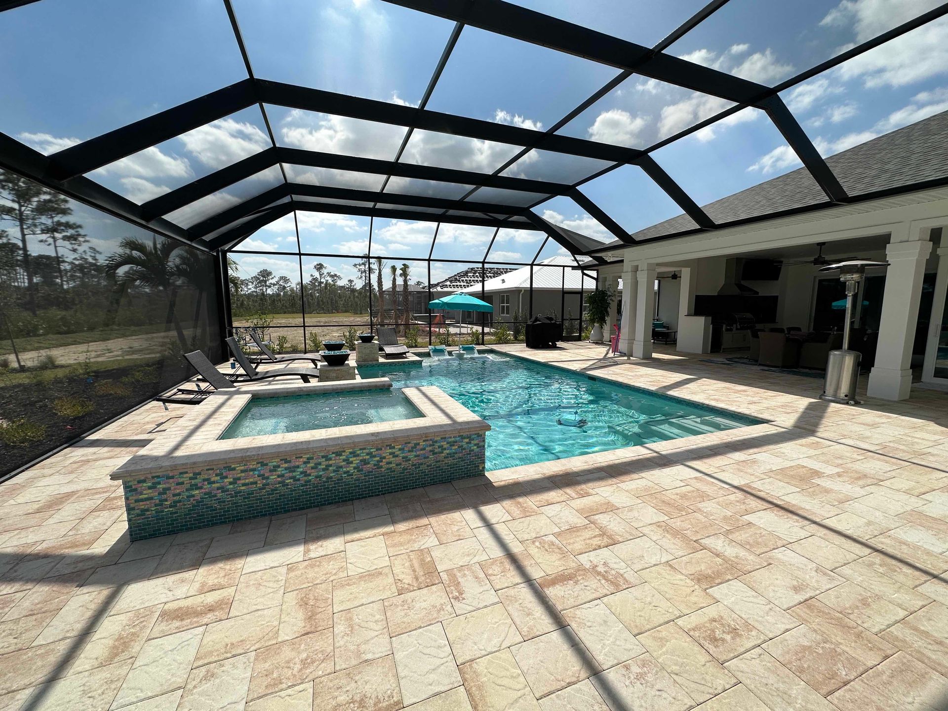 Pool and spa under a screened enclosure. Turquoise water, tan patio, blue umbrella, and blue and white tiles.