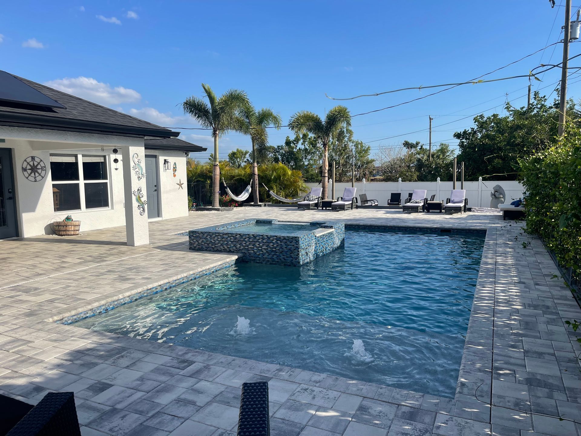 Poolside scene with a pool, jacuzzi, palm trees, and lounge chairs under a clear blue sky.
