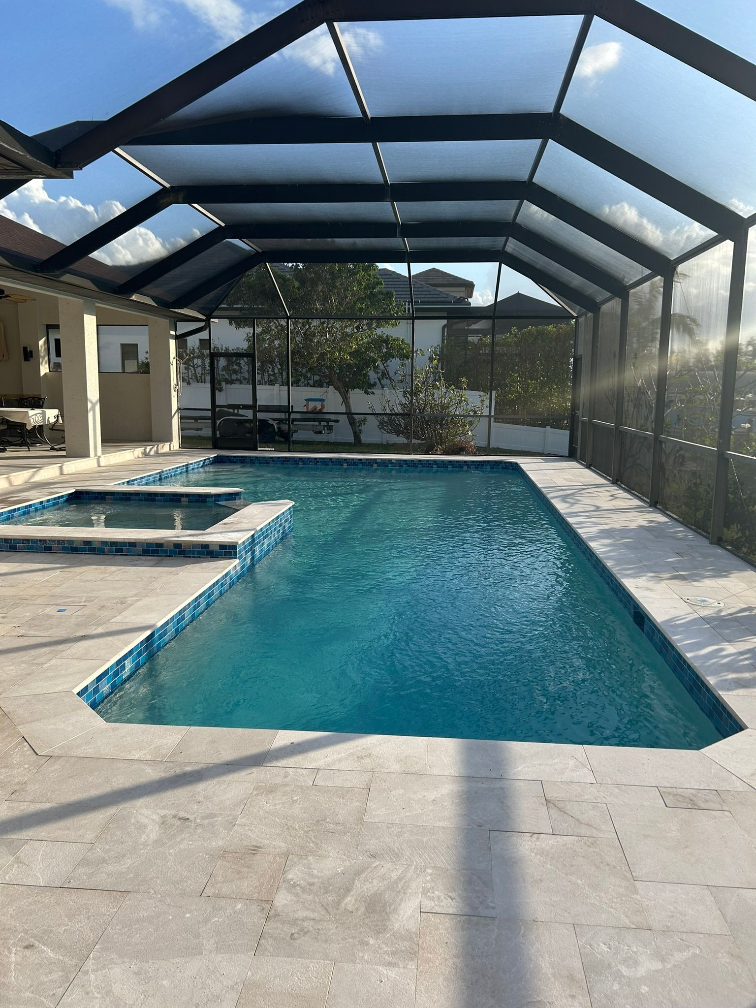 A screened-in swimming pool with a hot tub in a sunny backyard setting.