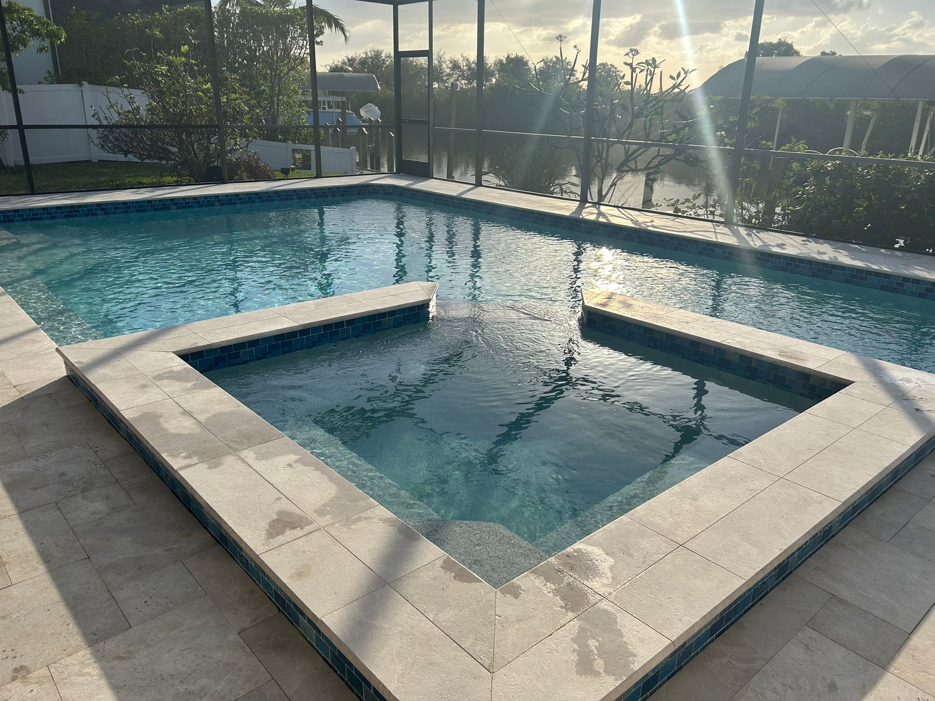 Pool with built-in spa; aqua water, stone deck, screened enclosure, sunny outdoors.