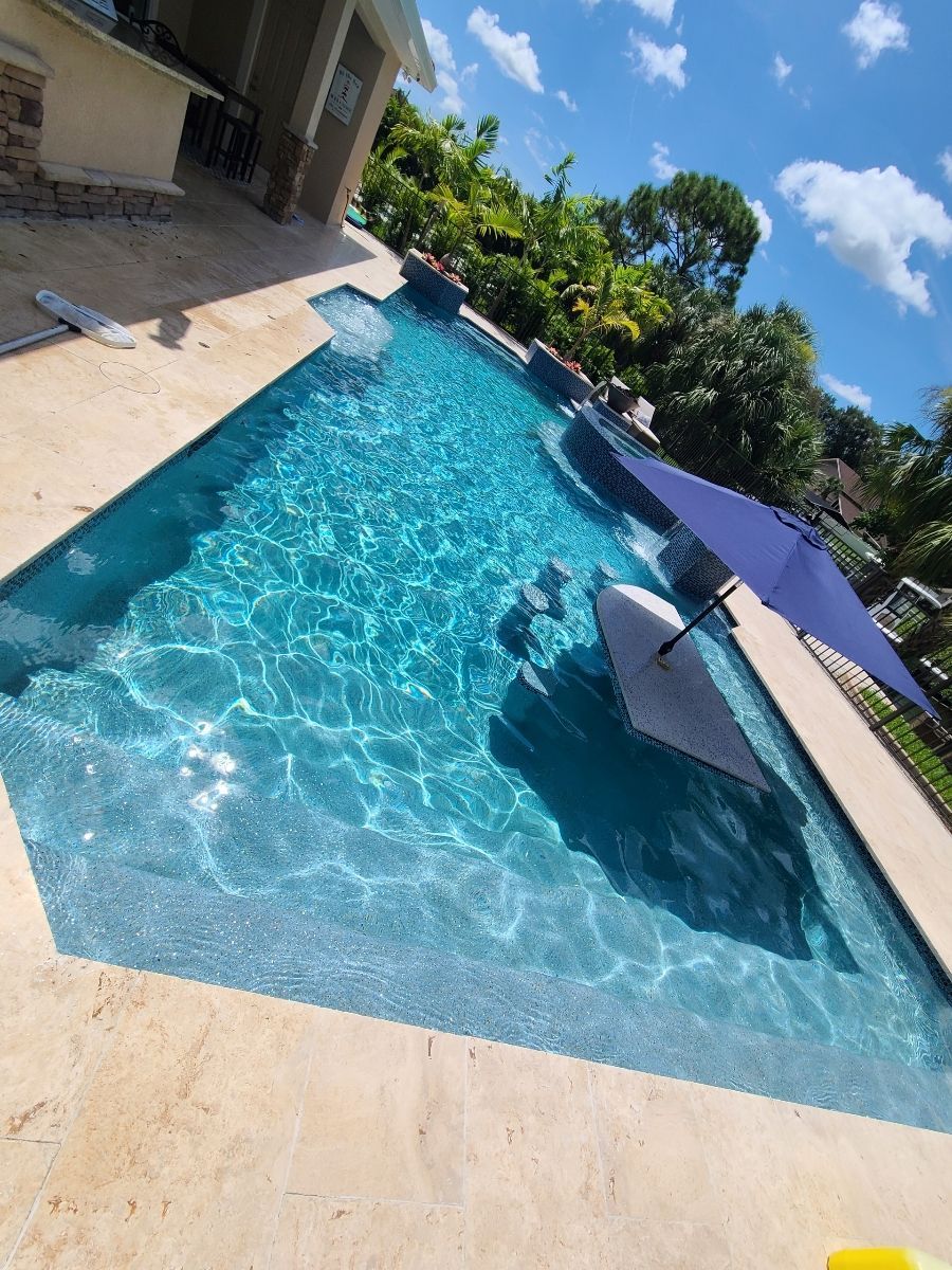 Blue-tiled swimming pool with a tan deck under a bright sky.