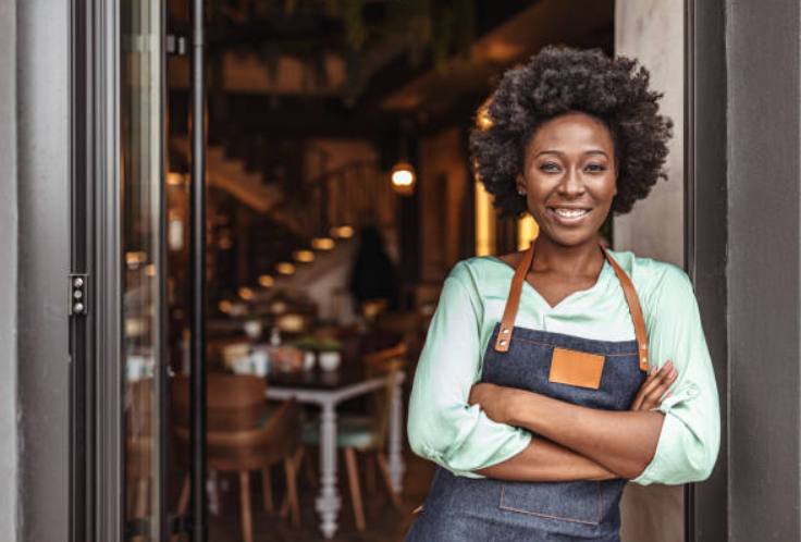 A woman in an apron is standing in the doorway of a restaurant.