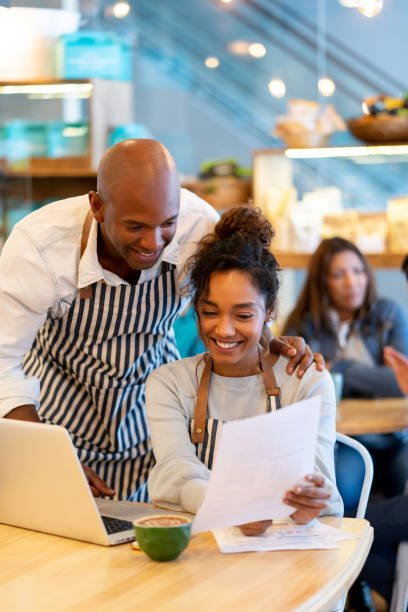 A man and a woman are sitting at a table in a restaurant looking at a laptop.