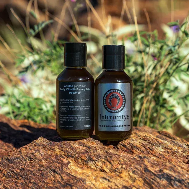 Two amber bottles of Interrentye body oil sit on a rough stone surface against a background of desert foliage.