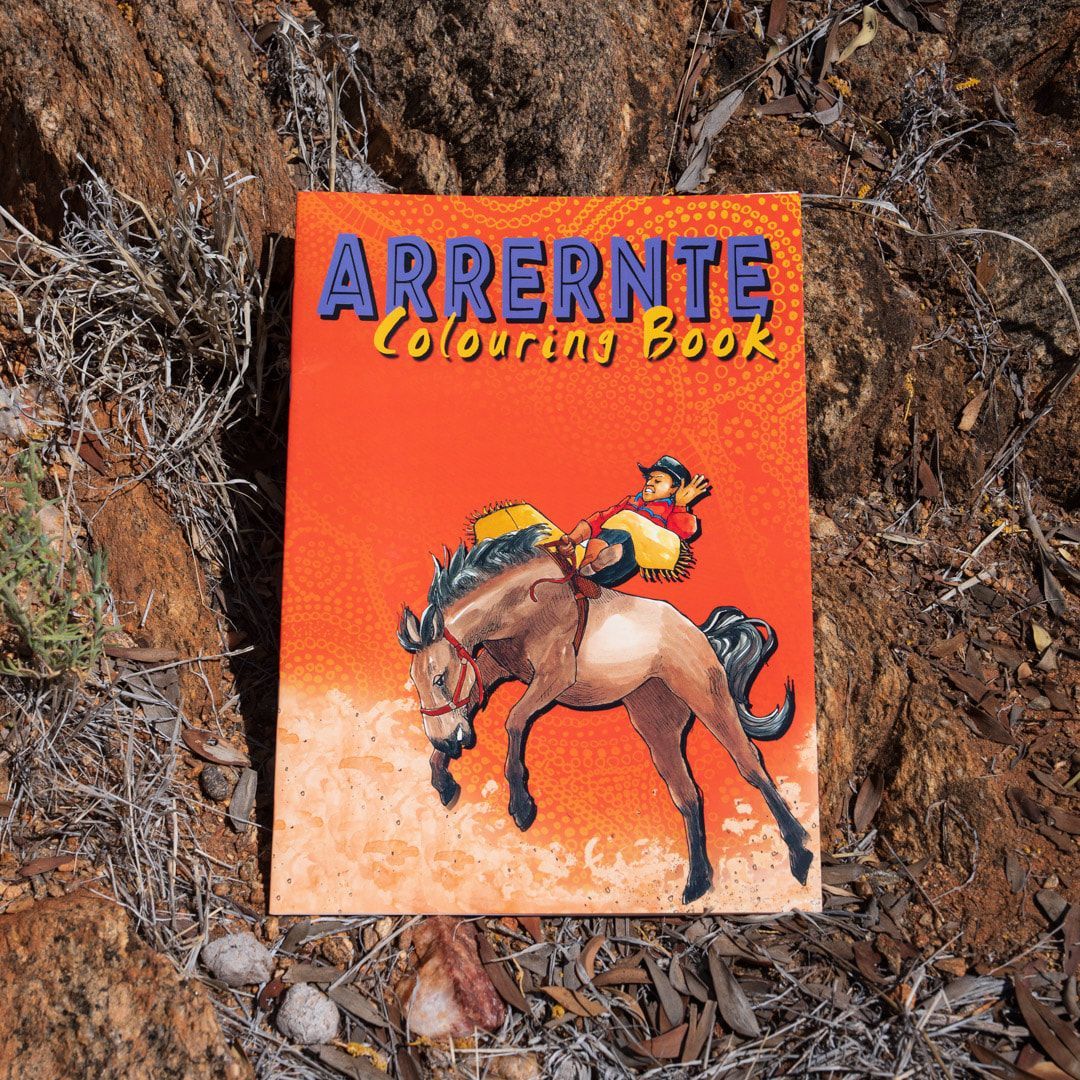An Arrernte colouring book with an illustration of a rider on a bucking horse, set against a rocky background.
