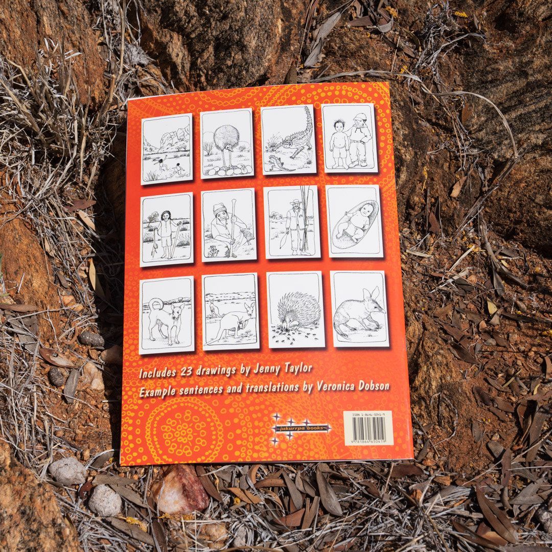 An Arrernte colouring book with an illustration of a rider on a bucking horse, set against a rocky background.