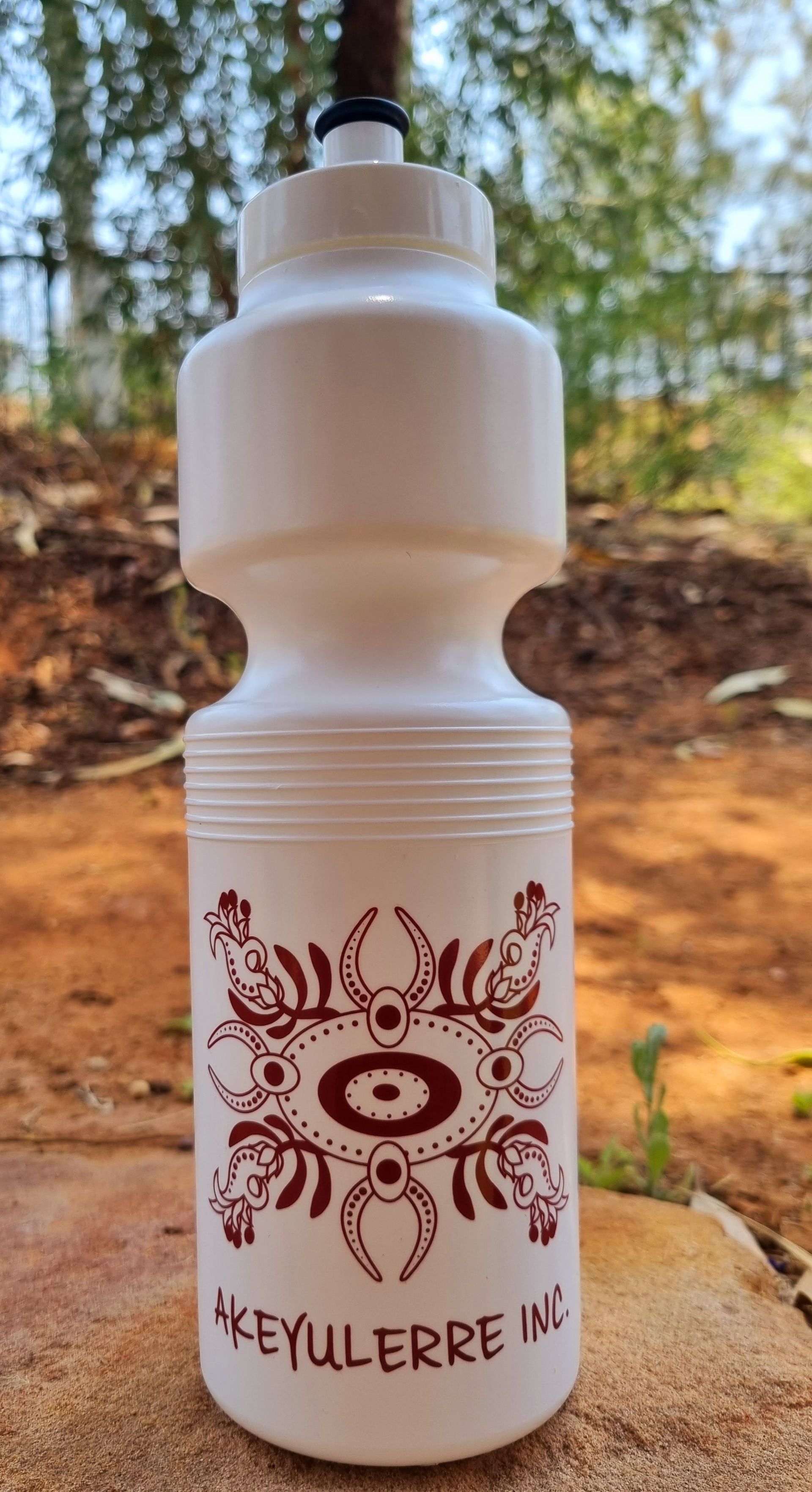 A white plastic squeeze water bottle featuring a red, circular indigenous-style design and the text 