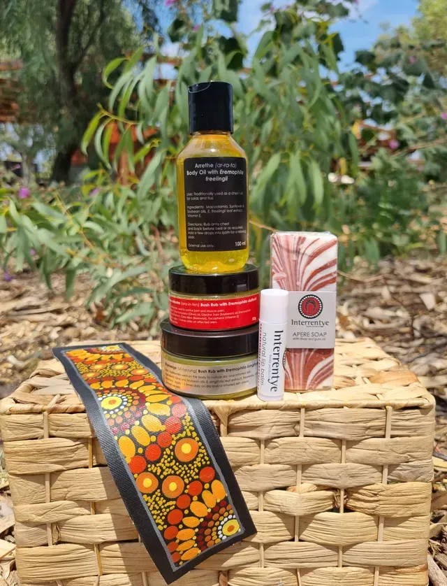 Skincare products and a patterned fabric strip arranged on a woven basket outdoors among plants.