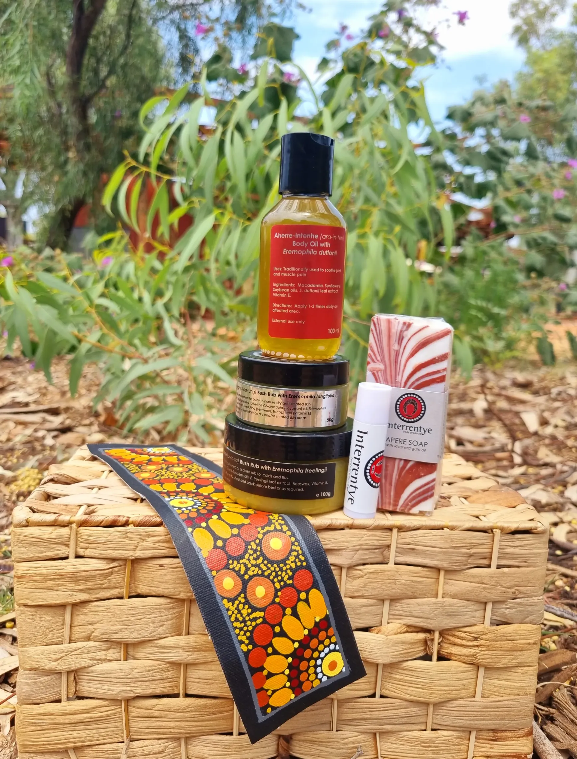 A collection of skincare products arranged on a woven basket against a background of green foliage and mulch.