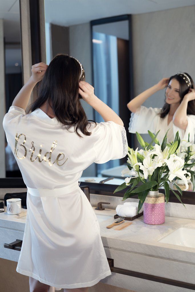 A woman in a white robe is brushing her hair in front of a mirror.