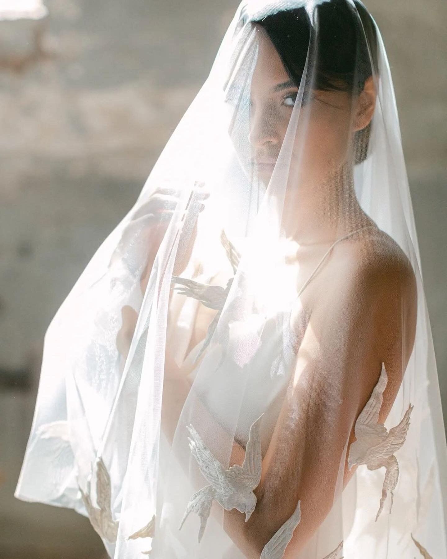 A woman in a wedding dress is covering her face with a veil.