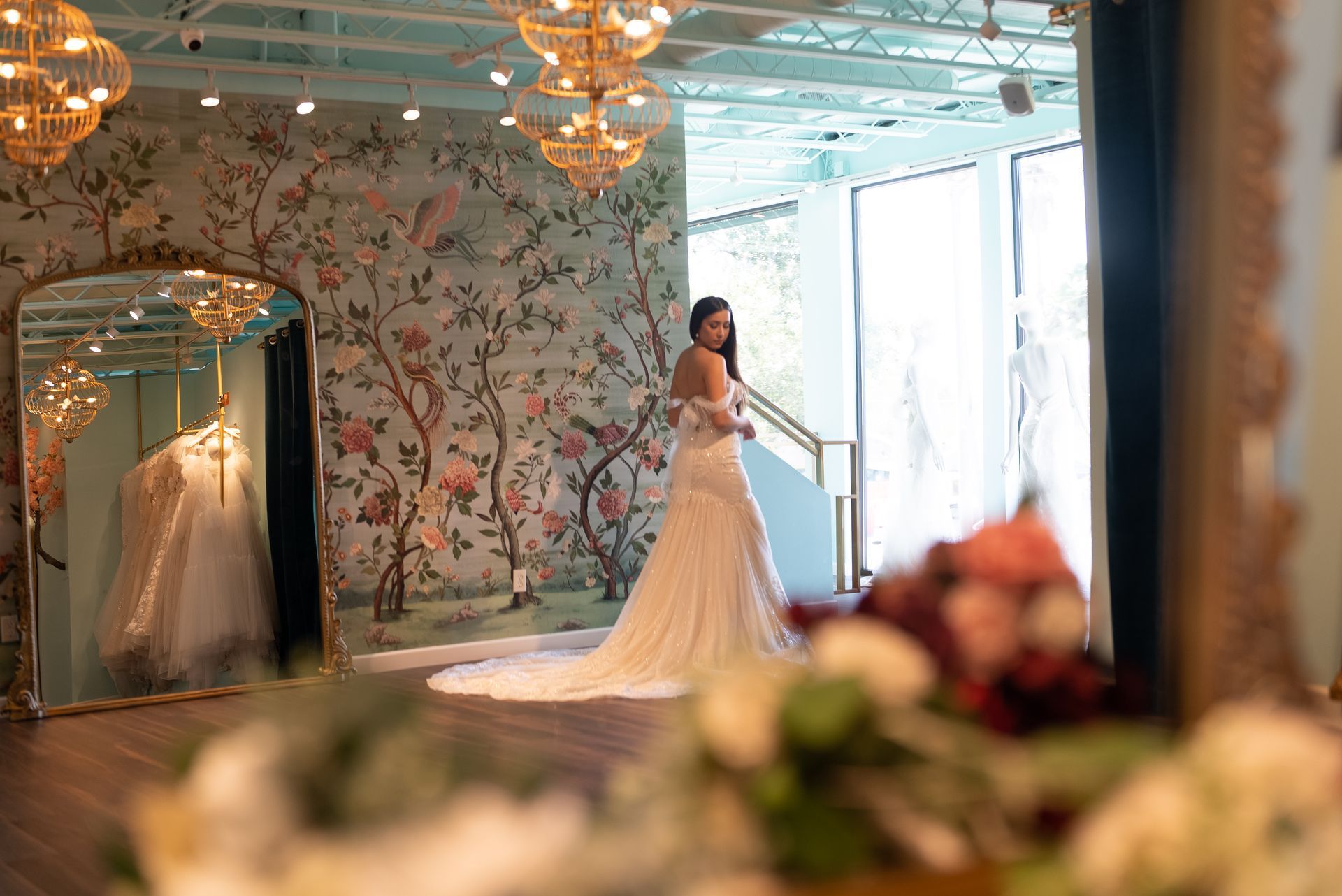 A woman in a wedding dress is standing in front of a mirror in a bridal shop.