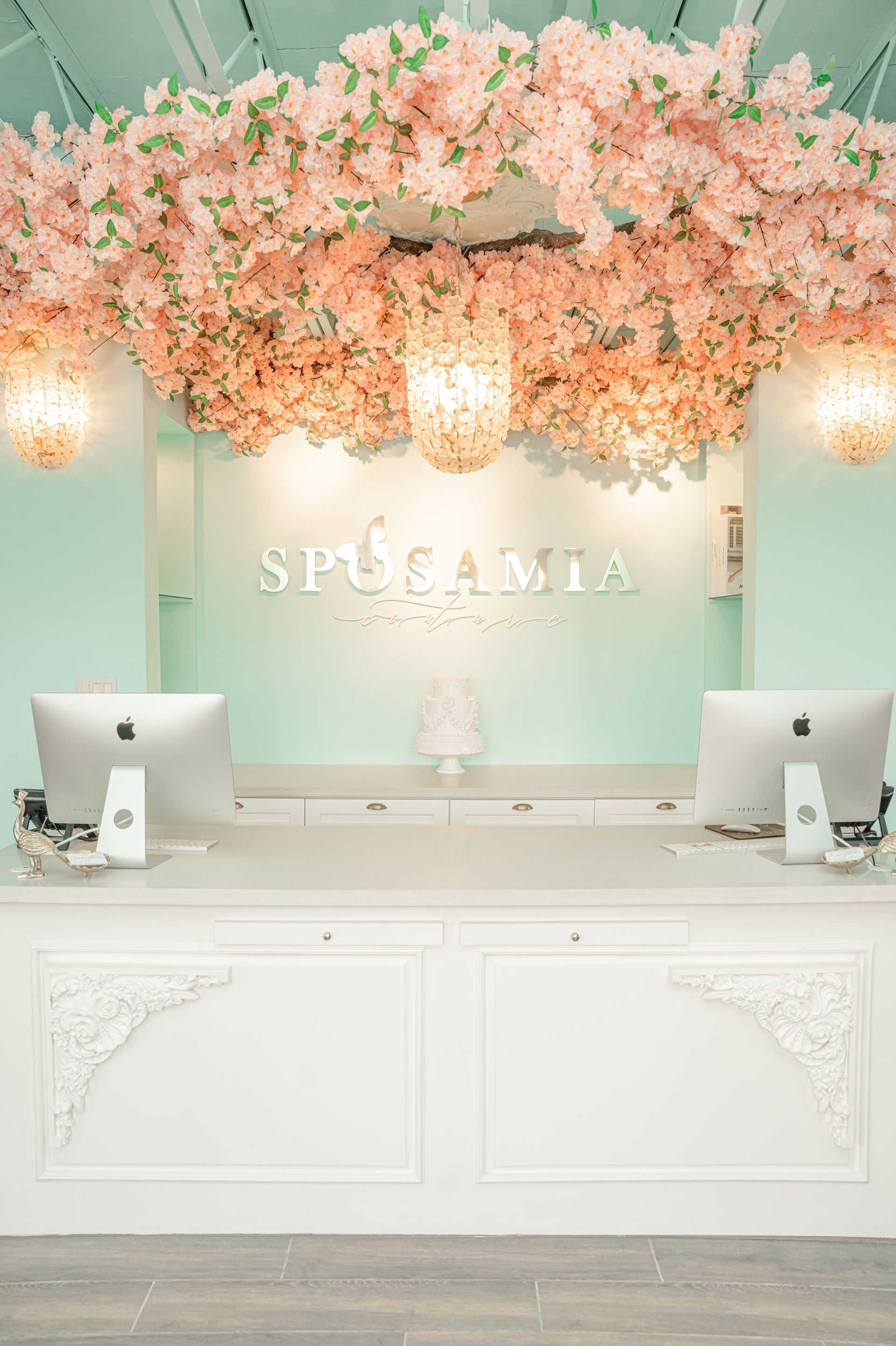 A reception desk in a store with pink flowers hanging from the ceiling.
