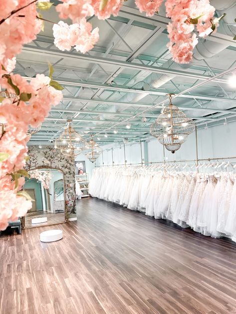 A large room filled with lots of white dresses and pink flowers.