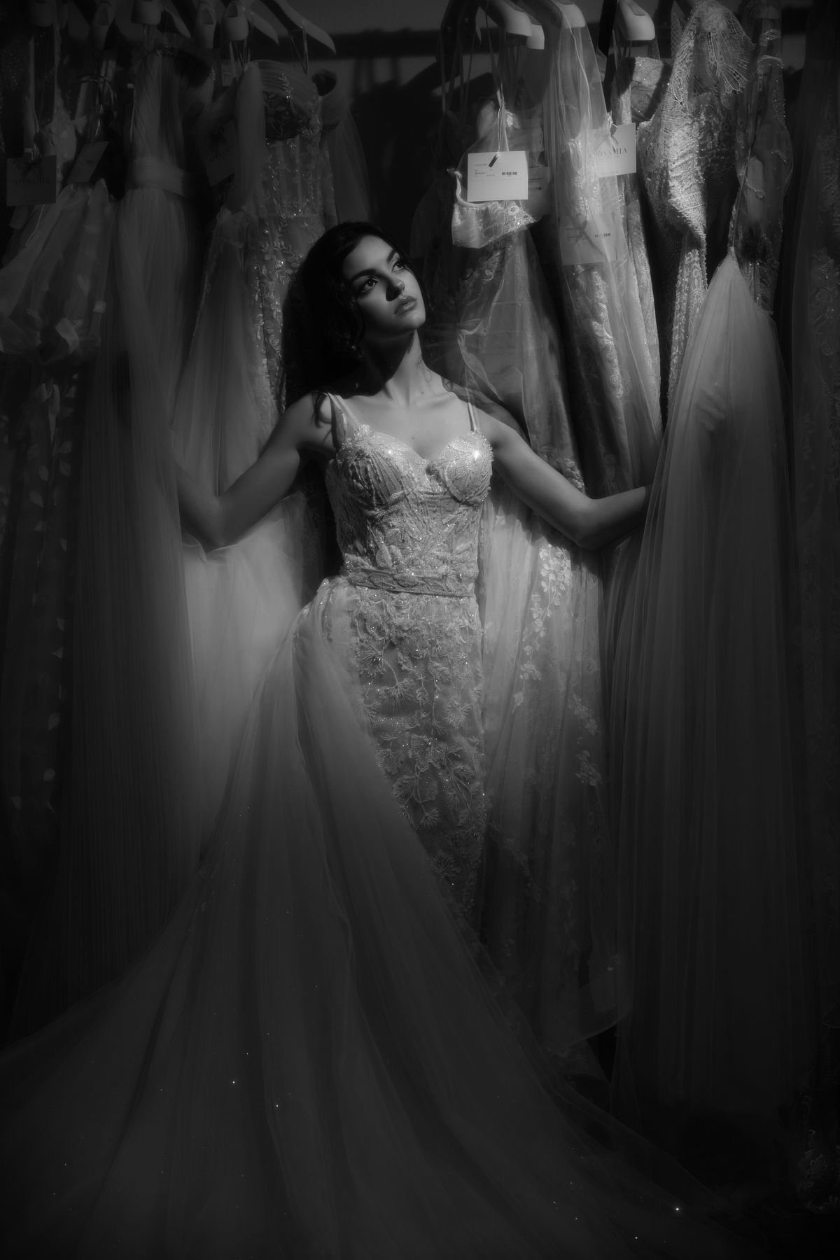 A woman in a wedding dress is standing in front of a row of wedding dresses.
