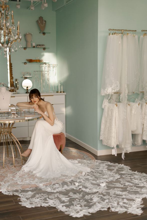 A woman in a wedding dress is sitting on a stool in a room.