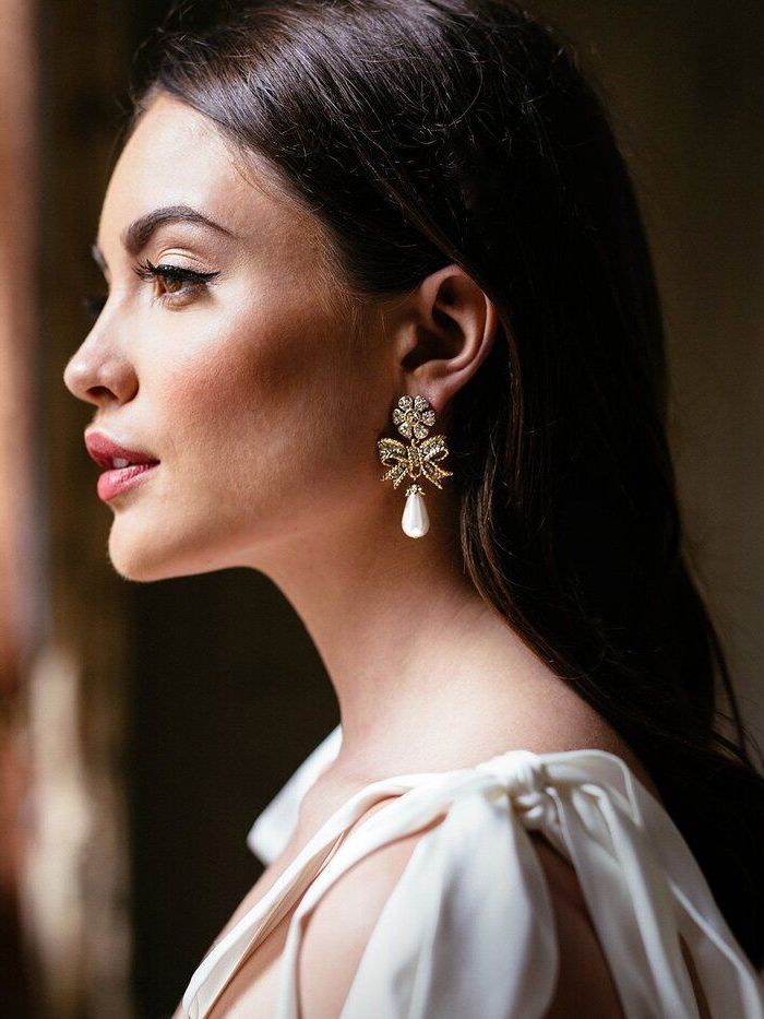 A woman in a white dress is wearing a pair of earrings.