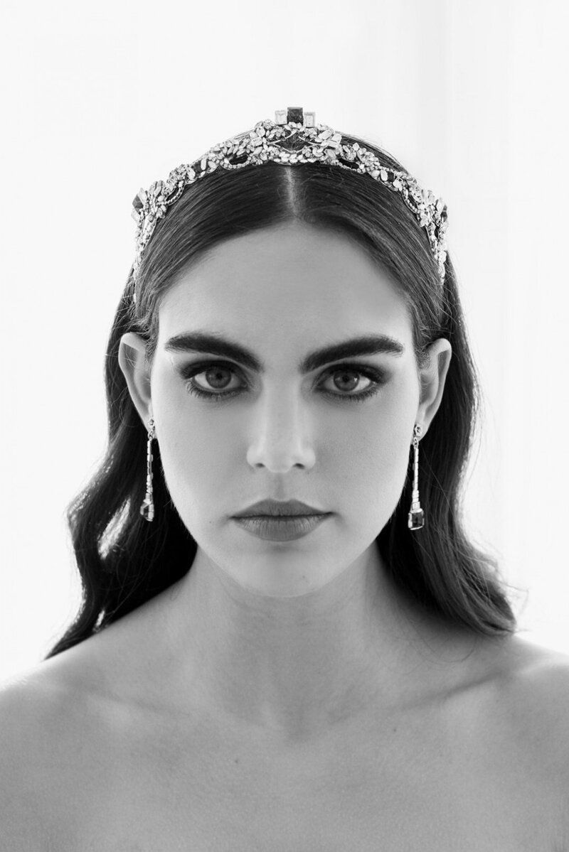 A black and white photo of a woman wearing a tiara and earrings