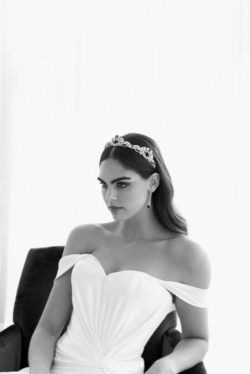 A woman in a wedding dress and tiara is sitting in a chair.