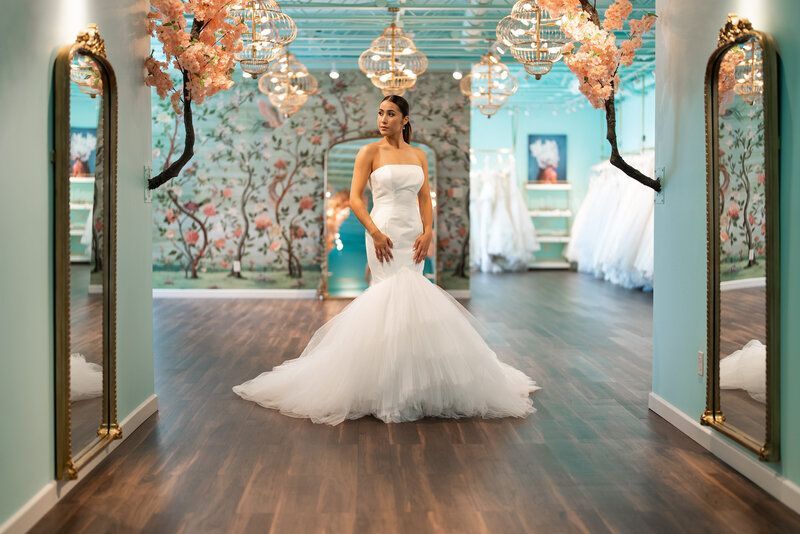 A woman in a wedding dress is standing in front of a mirror in a bridal shop.