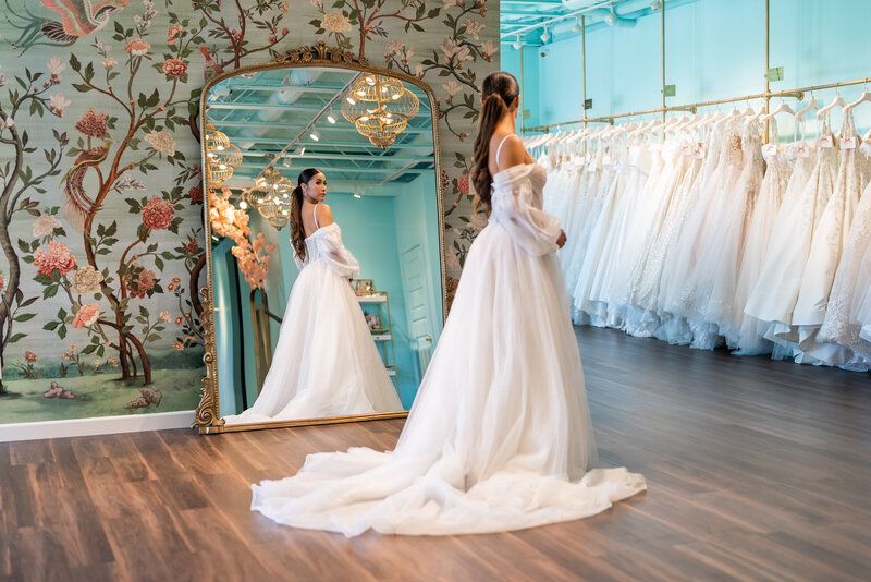 A woman in a wedding dress is standing in front of a mirror in a bridal shop.