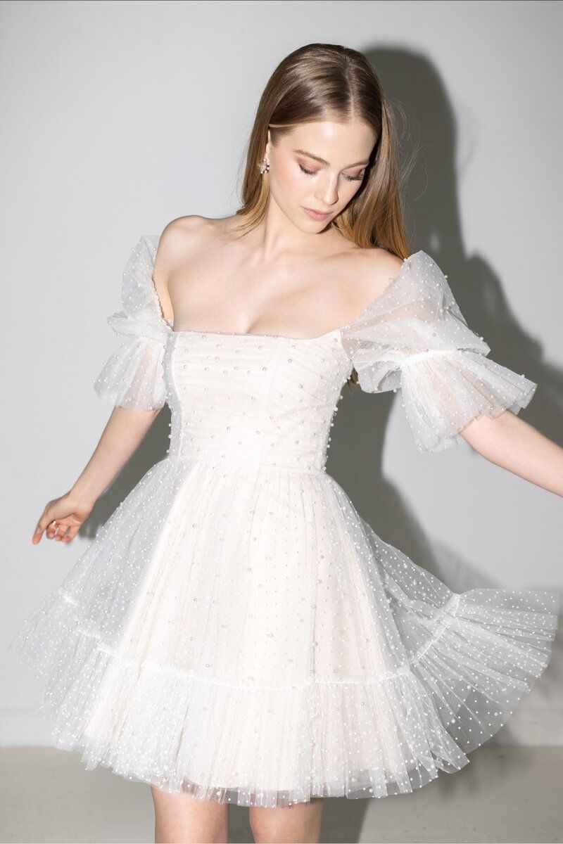 A woman is wearing a white dress with polka dots and ruffled sleeves.