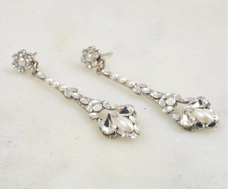 A pair of earrings with pearls and rhinestones on a white surface