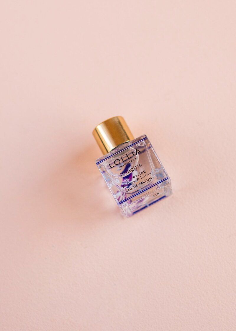 A small bottle of perfume is sitting on a pink surface.