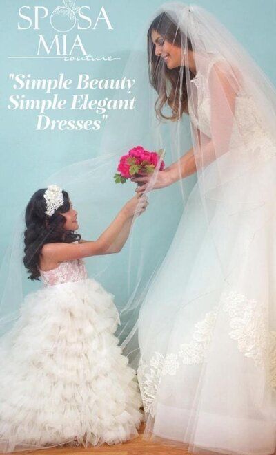 A woman in a wedding dress is giving a flower to a little girl in a white dress