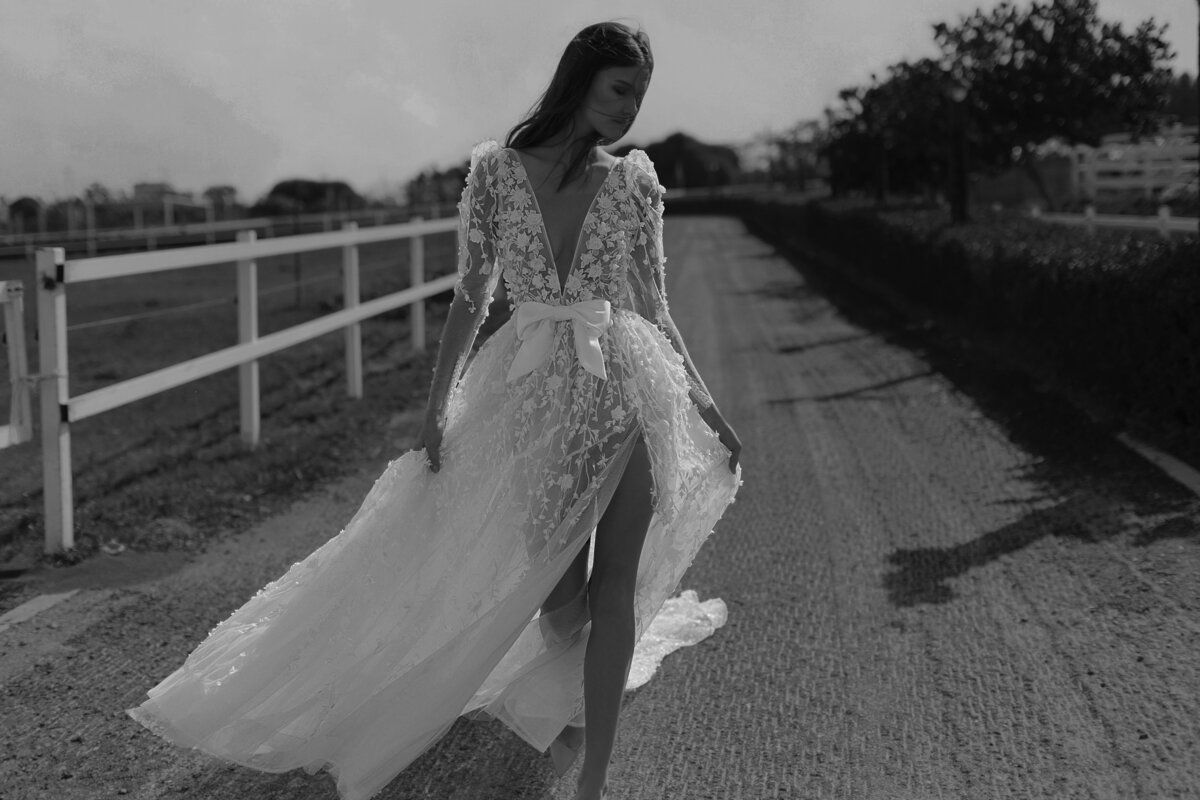 A black and white photo of a woman in a wedding dress walking down a road.