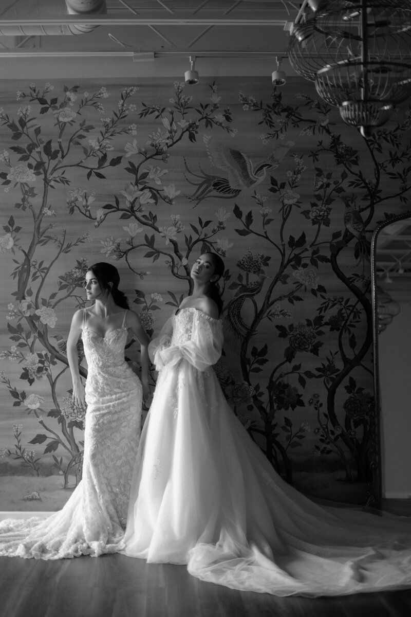 Two women in wedding dresses are standing next to each other in a room.