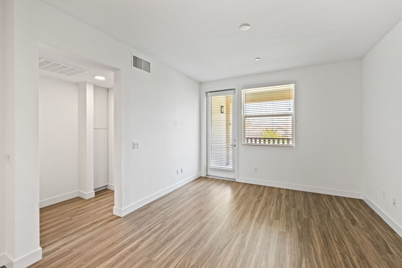 Empty living area with wood-like flooring, white walls, and a glass door with blinds.