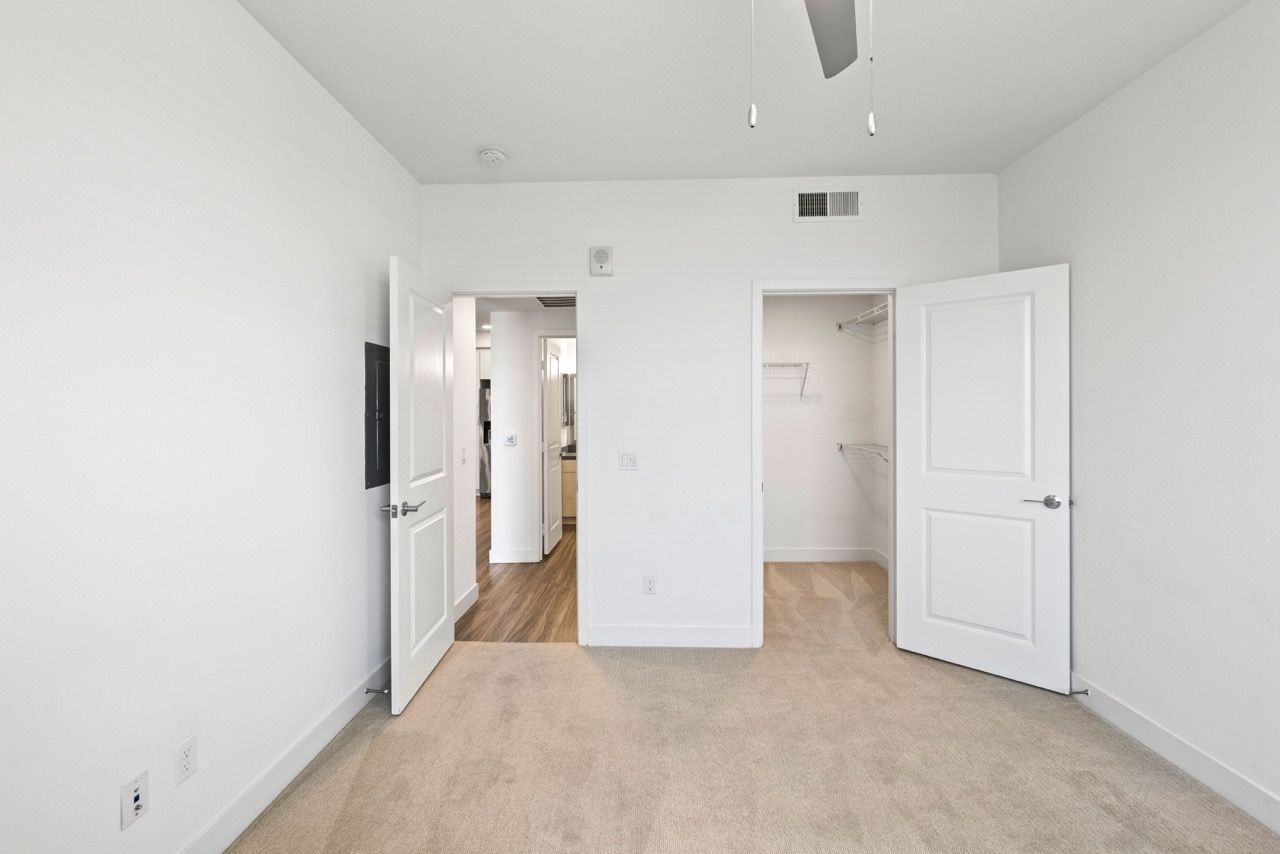 Empty bedroom with beige carpet, white walls, and an open closet with wire shelving.