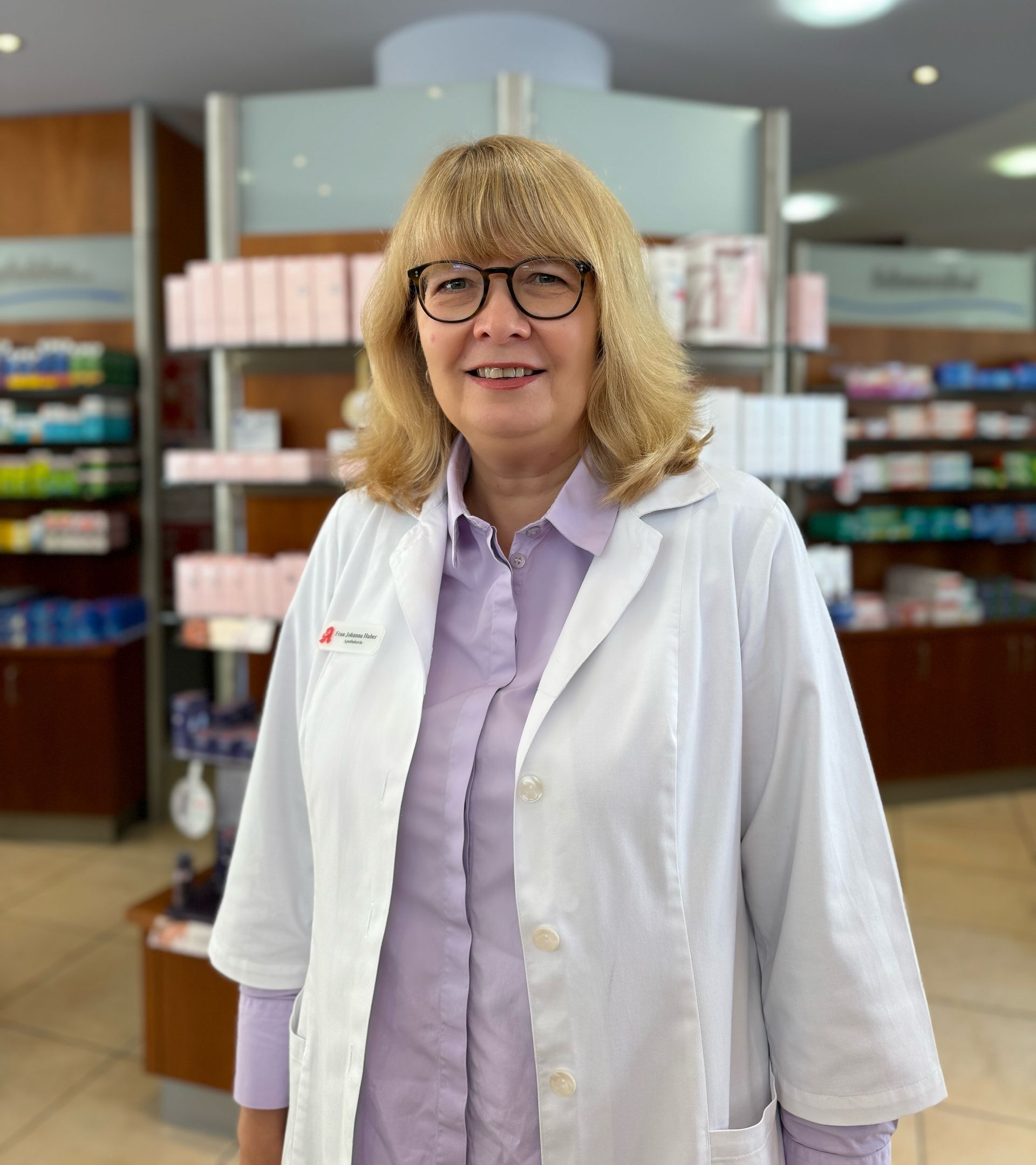 Eine Frau mit Brille und weißem Kittel steht in einer Apotheke.