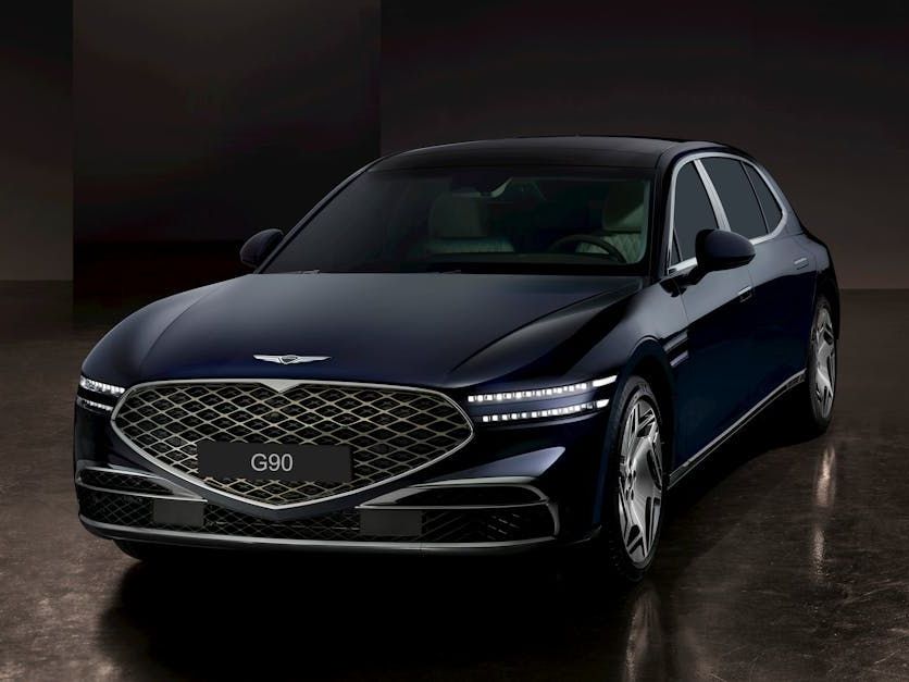 Blue Genesis G90 sedan parked in a studio. Features a large grille and sleek headlights.