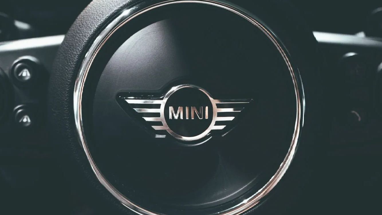 Close-up of a Mini Cooper steering wheel, black with a silver MINI logo in the center.