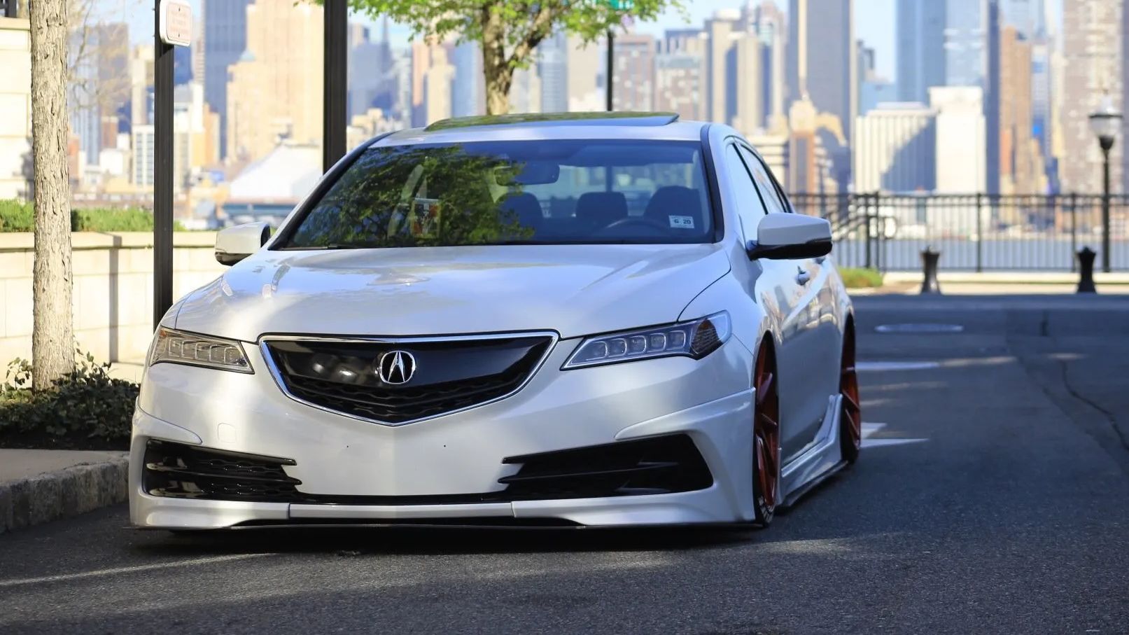 White Acura sedan parked on a city street, with a skyline in the background.