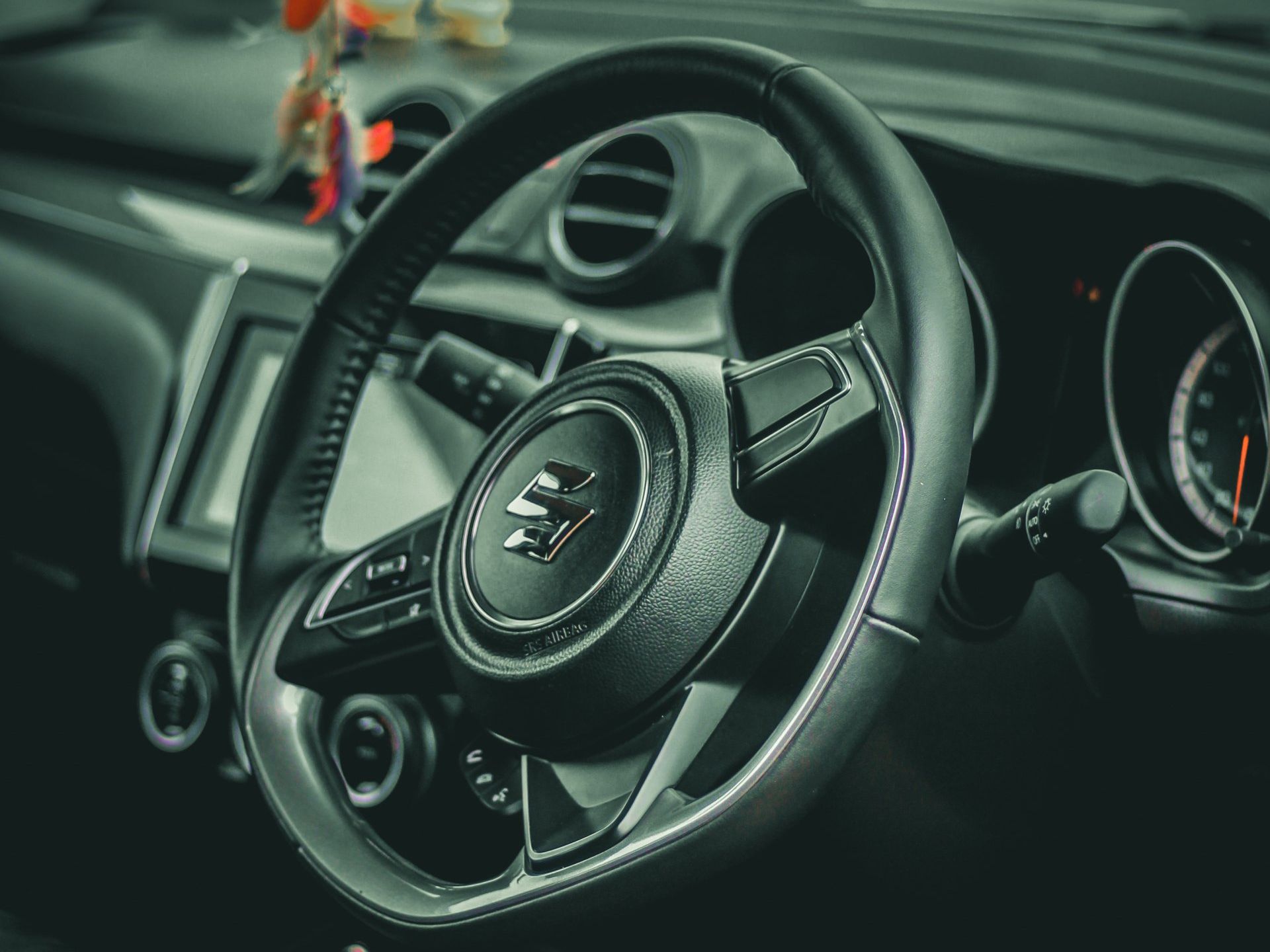 Black Suzuki car steering wheel with controls and dashboard details.