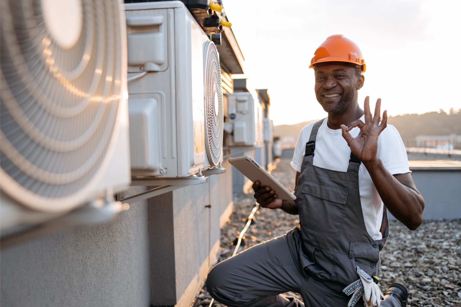 HVAC technician wearing mask and hard hat, working on AC units on a rooftop.