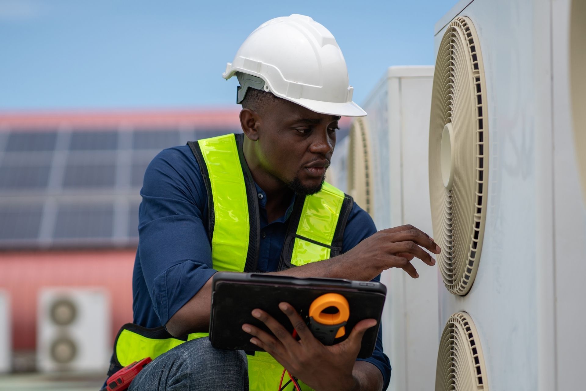 HVAC technician wearing mask and hard hat, working on AC units on a rooftop.