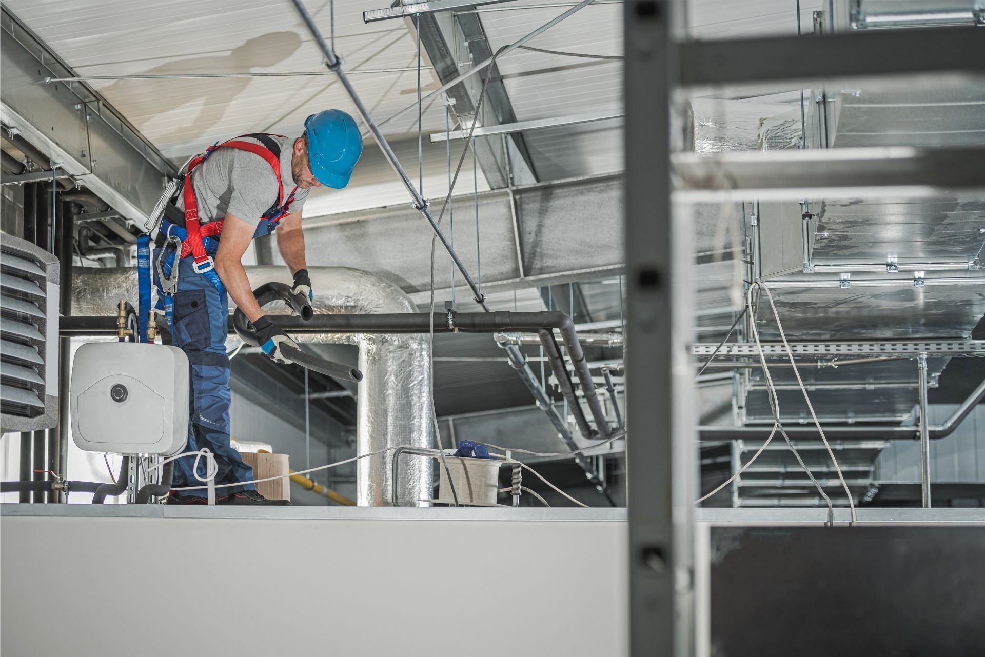HVAC technician wearing mask and hard hat, working on AC units on a rooftop.