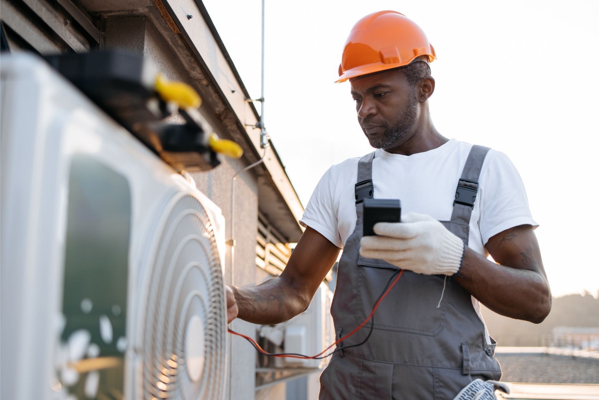 HVAC technician wearing mask and hard hat, working on AC units on a rooftop. HVAC technician wearing mask and hard hat, working on AC units on a rooftop.