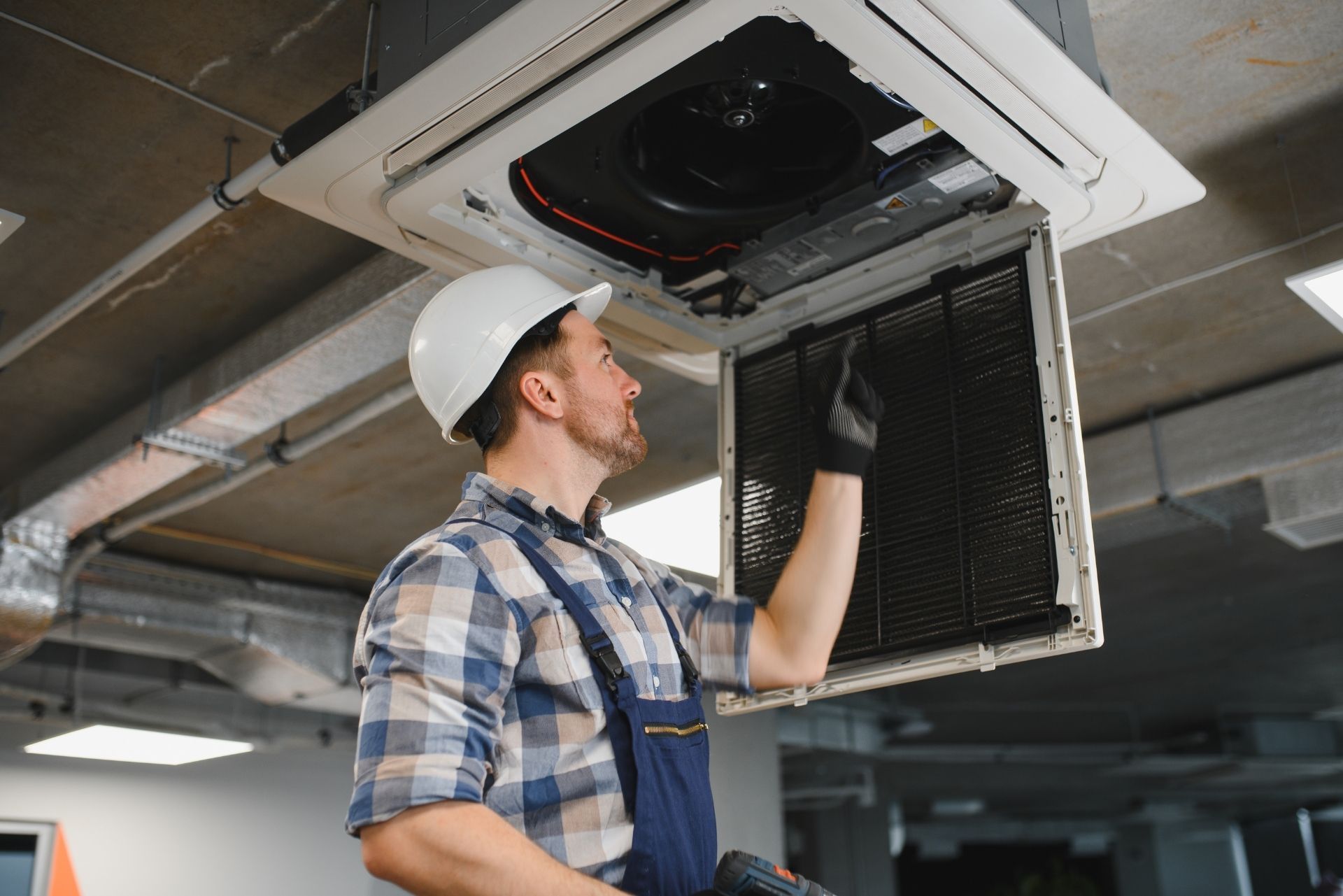 HVAC technician wearing mask and hard hat, working on AC units on a rooftop. HVAC technician wearing mask and hard hat, working on AC units on a rooftop.
