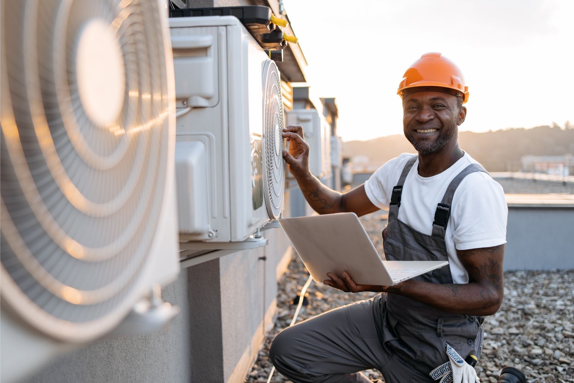 HVAC technician wearing mask and hard hat, working on AC units on a rooftop.