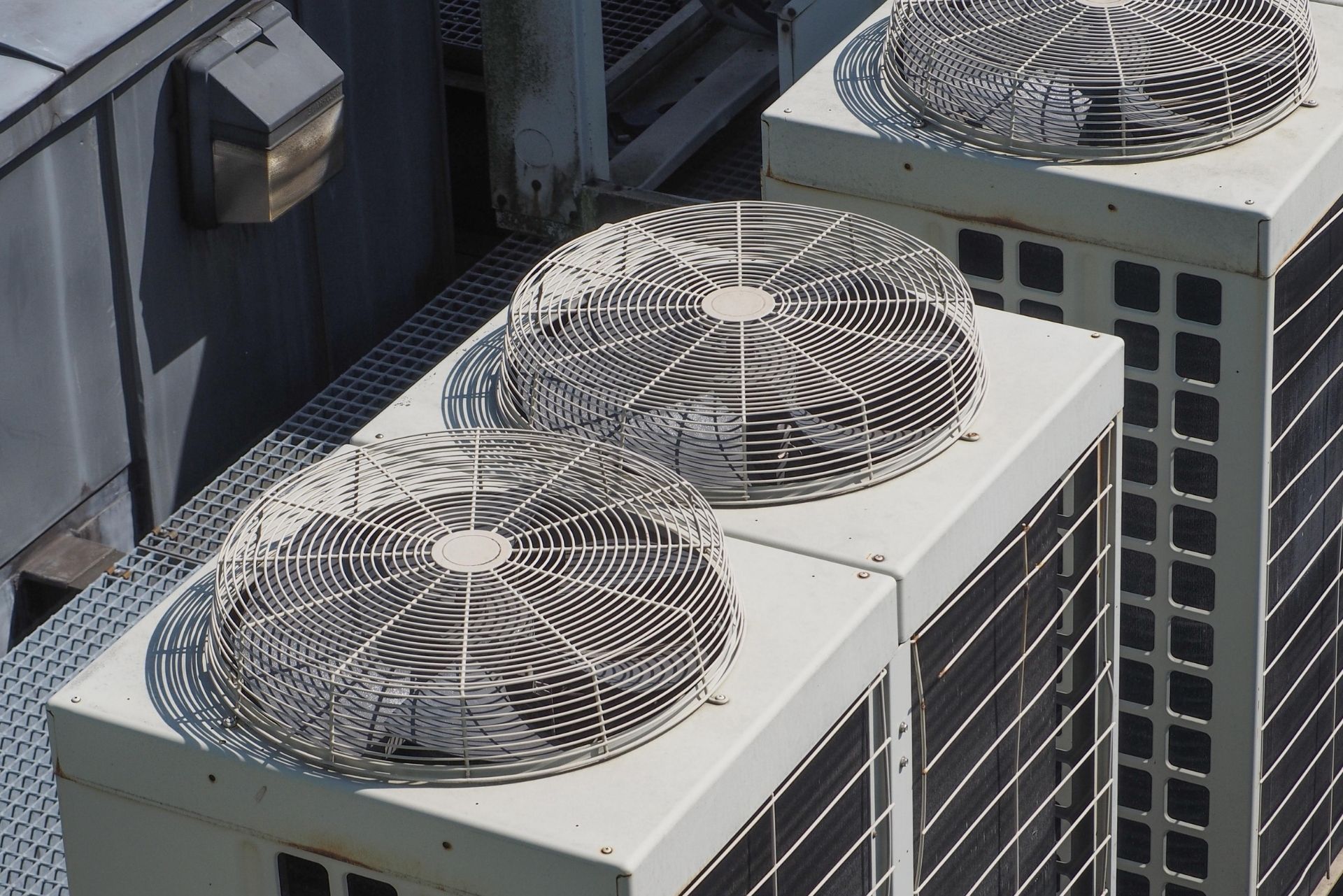 HVAC technician wearing mask and hard hat, working on AC units on a rooftop.